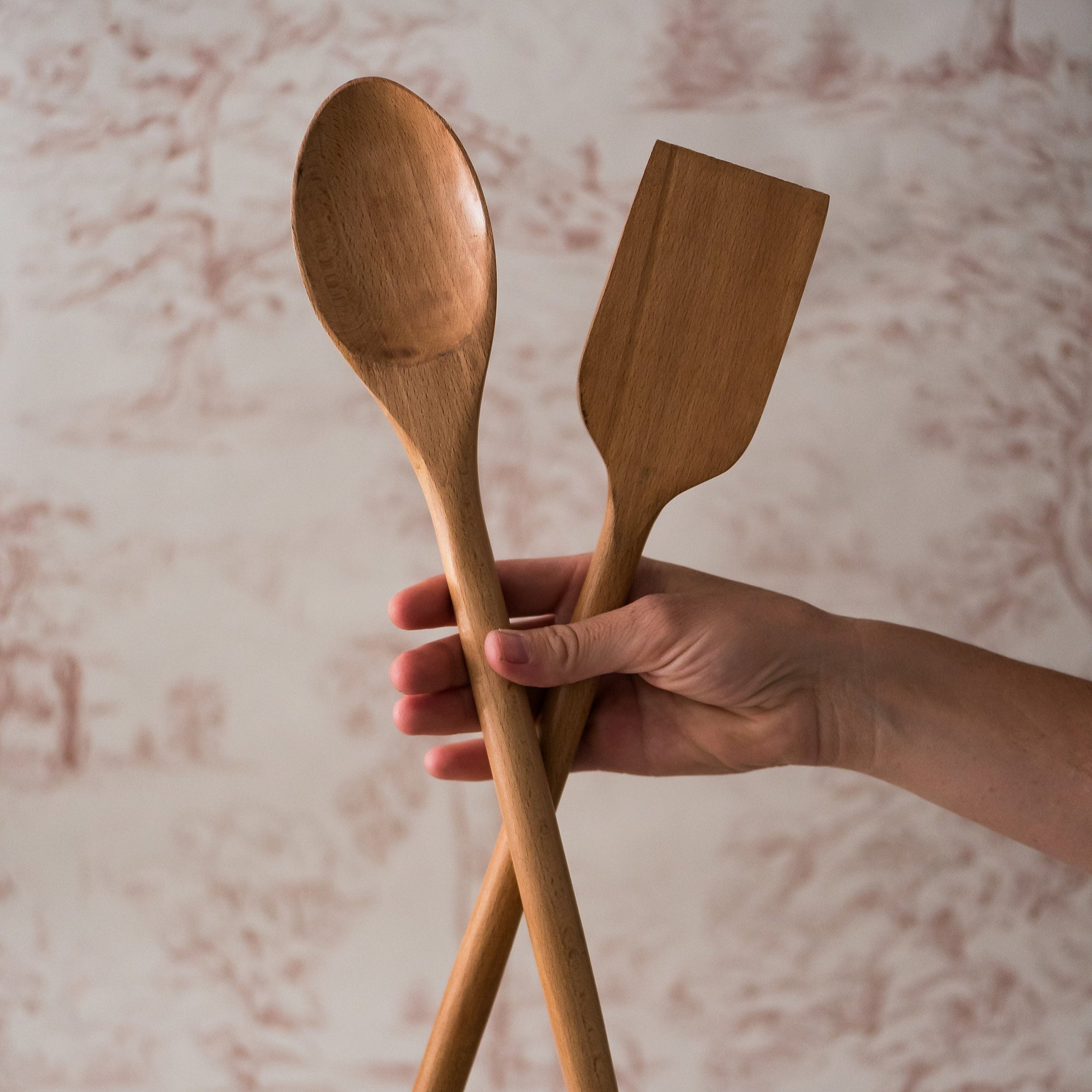 A person holding a wooden spoon and spatula against a textured background.